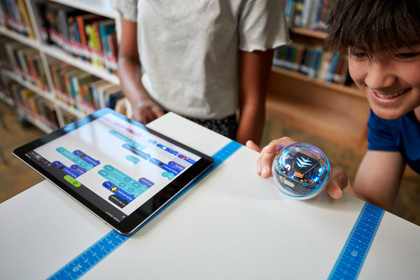 A student aims BOLT+. Next to the robot there is a tablet with code.