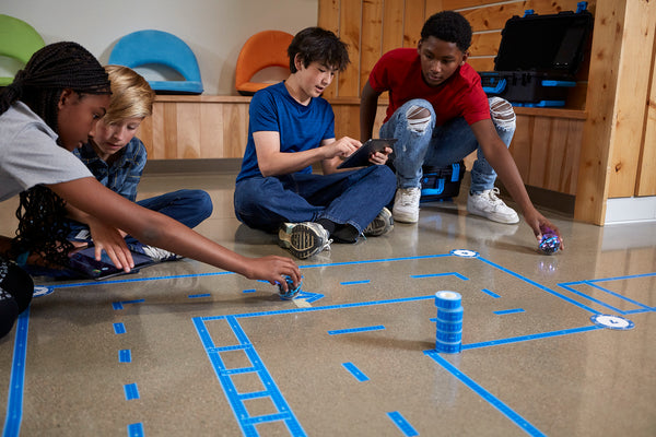 Students program their BOLT+ robots to navigate a grid and maze on the floor of their school.