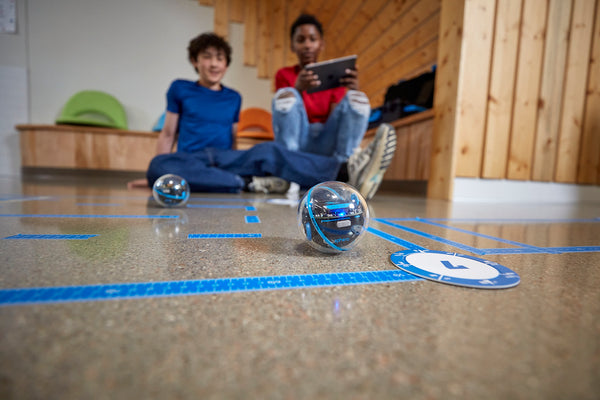 Two middle school students work on a program on a tablet to code Sphero BOLT+ through a maze.