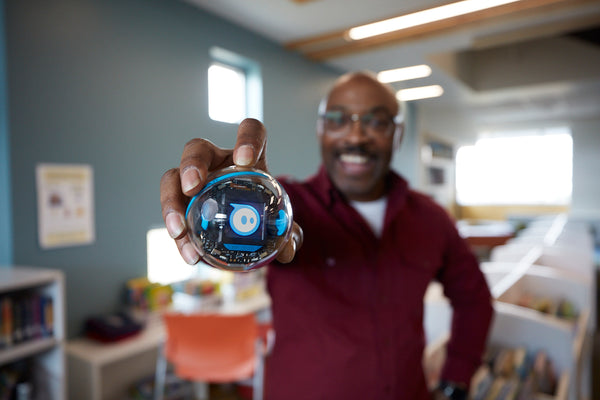 A teacher hold a BOLT+ robot with the Sphero logo displayed on the screen.