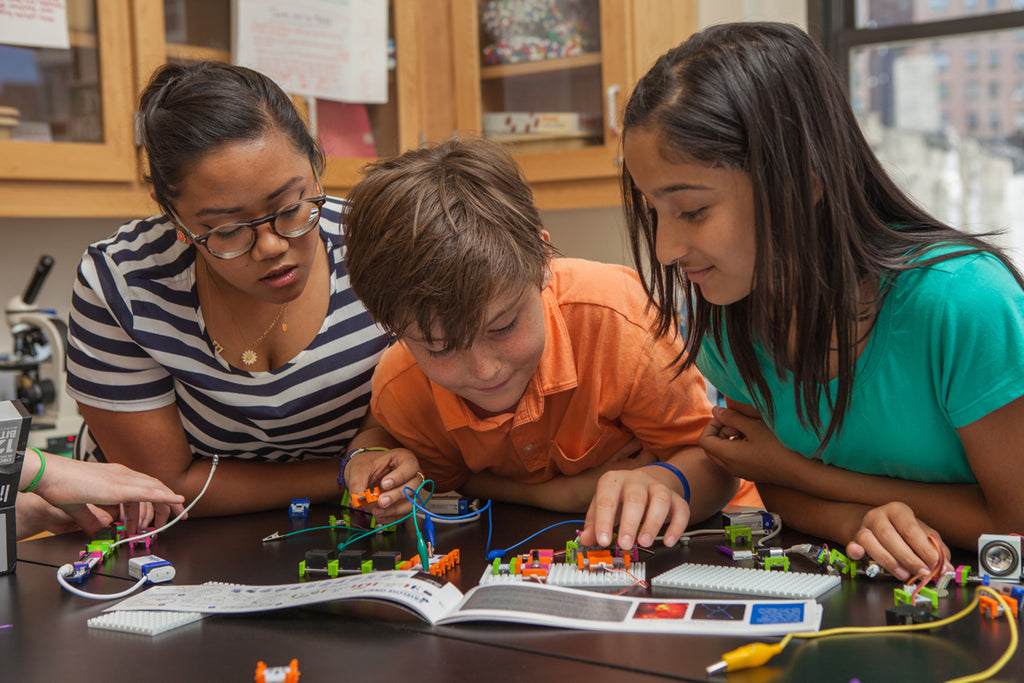 Three students look over a littleBits invention in their classroom.
