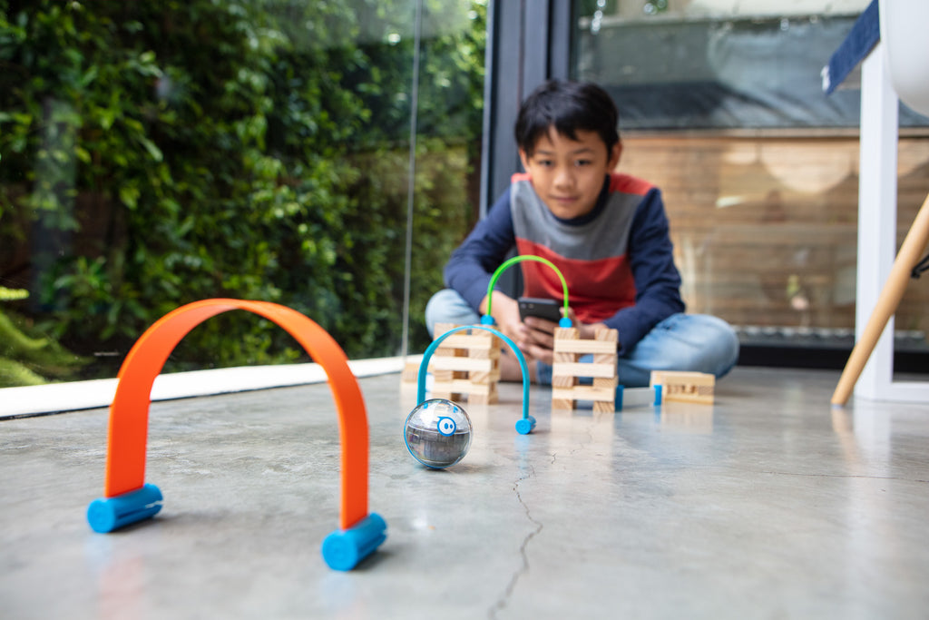 A kid sits on the ground and drives a Sphero Mini through an obstacle course.