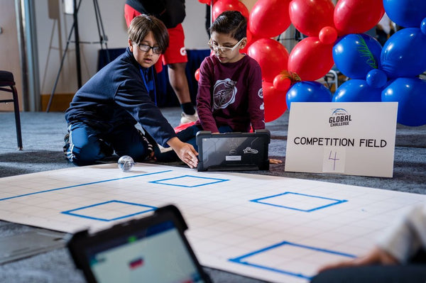 Two students code their robot on a competition field.