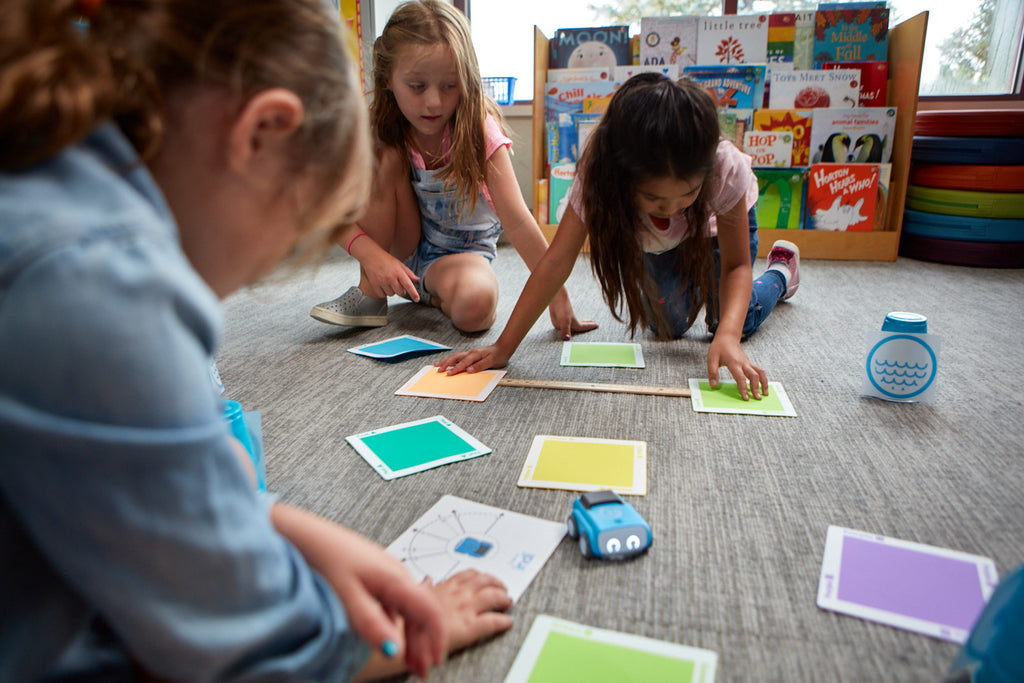 Three young students create a path using color tiles for Sphero indi..