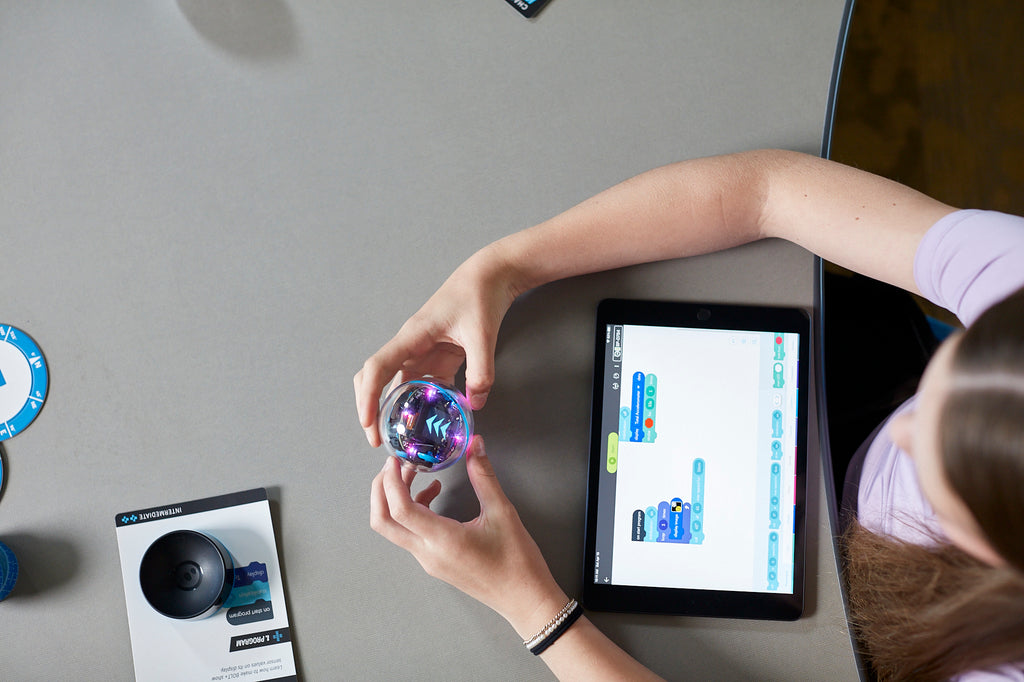 A student works on programming a Spheor BOLT+ robot in her classroom using the Sphero Edu app on a tablet.