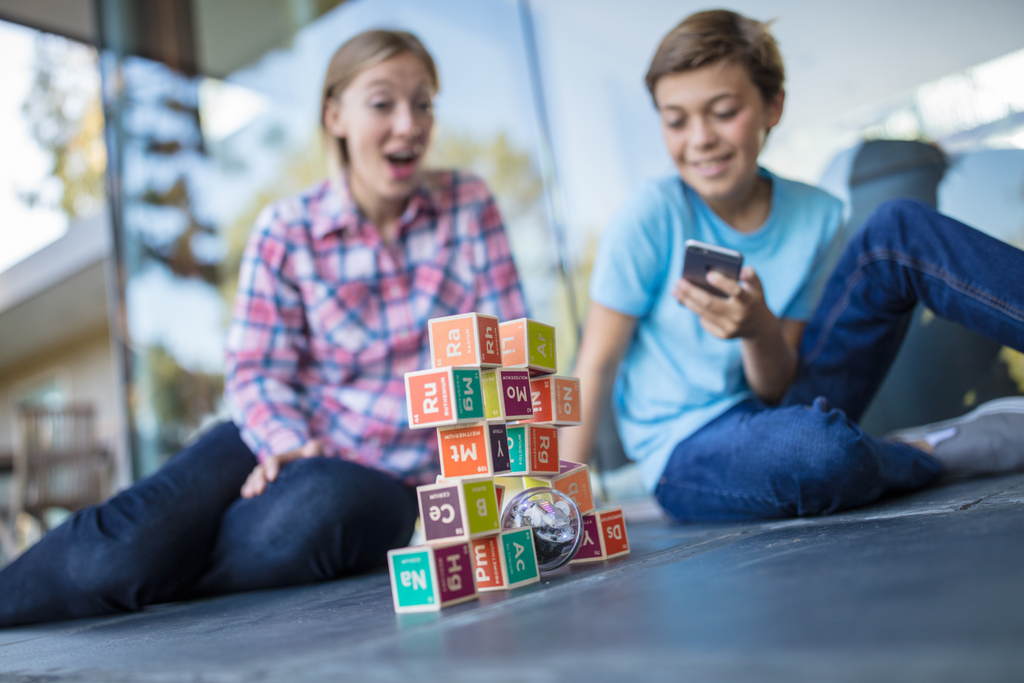 Two students knock down a tower of blocks with a Sphero BOLT.