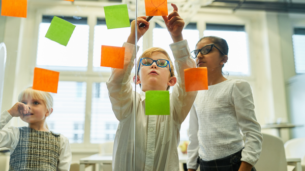 Three kids put sticky notes on a window in a classroom during a brainstorm session.
