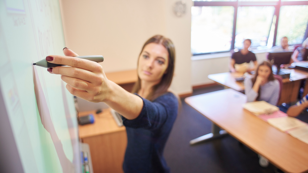 A woman writes on a Smartboard in front of a class of students.