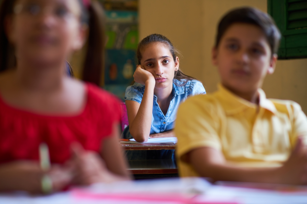 A student looking bored in the back of a classroom.
