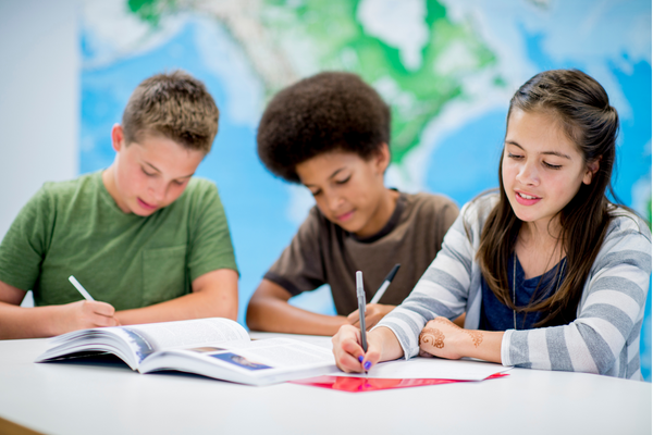 Three students take notes from a textbook.