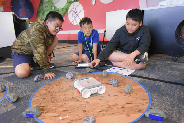 Three students code RVR+ through a Mars landscape.